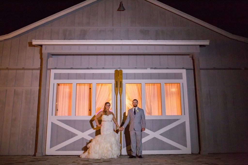 bride and groom holding hands in front of a grey barn