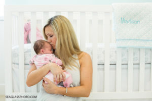 mom kisses baby girl on the forehead in the nursery with white pink and aqua