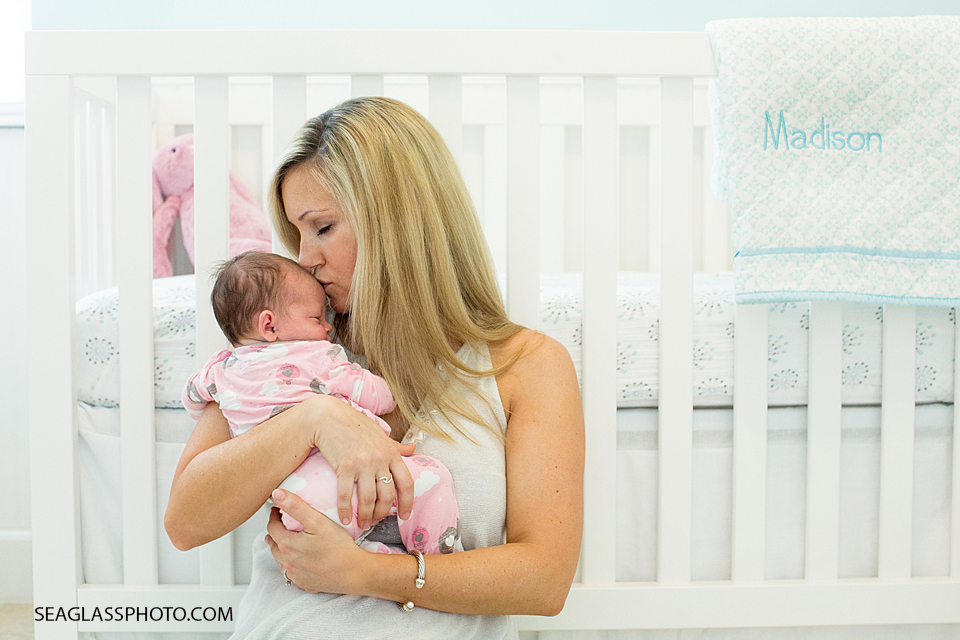 mom kisses baby girl on the forehead in the nursery with white pink and aqua