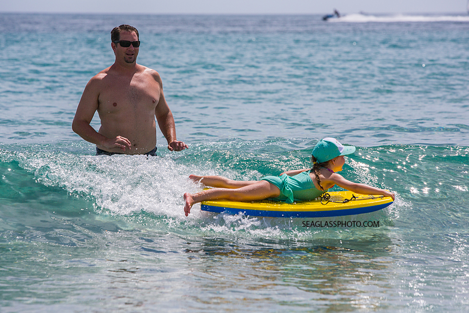 Father in the ocean with toddler girl catching a wave on her boogie board