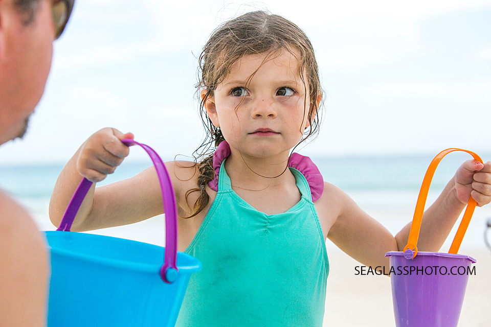 Toddler girl holding up two buckets at the beach. 