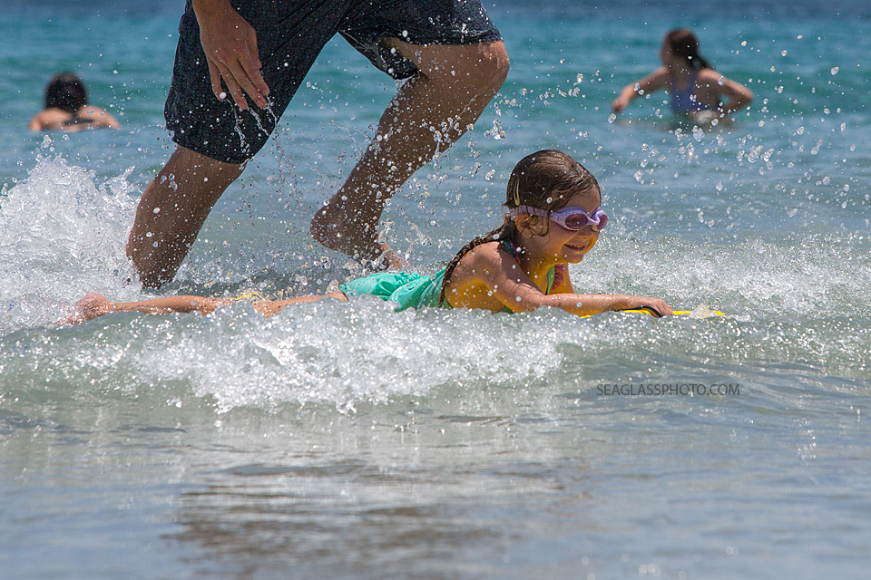 little girl catching a wave with her boogie board while her dad runs behind her in Vero Beach Florida 