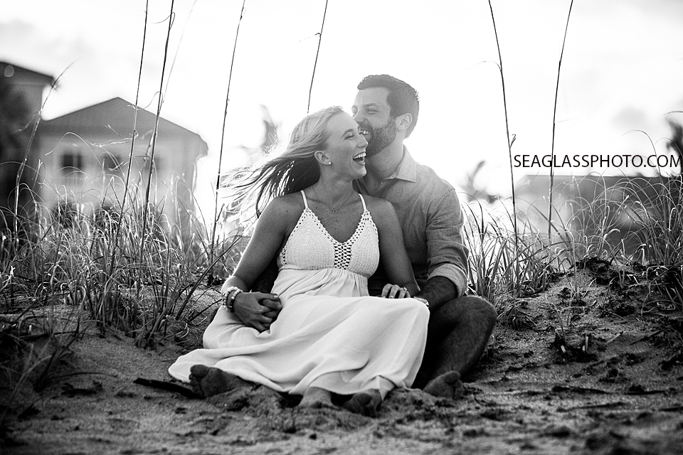 Black and white photo of couple sitting in the sand laughing in Vero Beach Florida