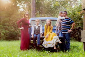 Family with three kids wearing fall colors sitting in an old blue truck in Vero Beach Florida