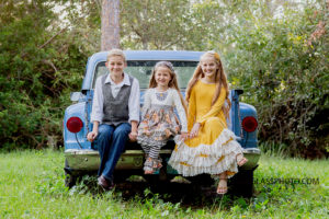 brother and two sisters wearing fall clothes sitting in an old blue truck in Vero Beach Florida