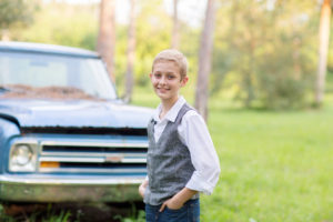 boy wearing grey vest in a field with an old blue truck in Vero Beach Florida