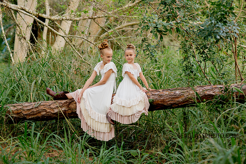 Sisters sitting on a log in a forest in Vero Beach Florida wearing boots and long cream dresses