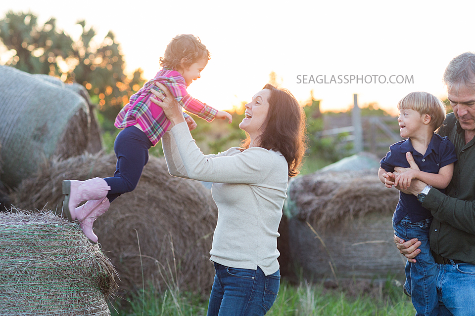 Girl with pink plaid and pink boots jumping off of a hay pile into her mom's arms at sunset in Vero Beach Florida
