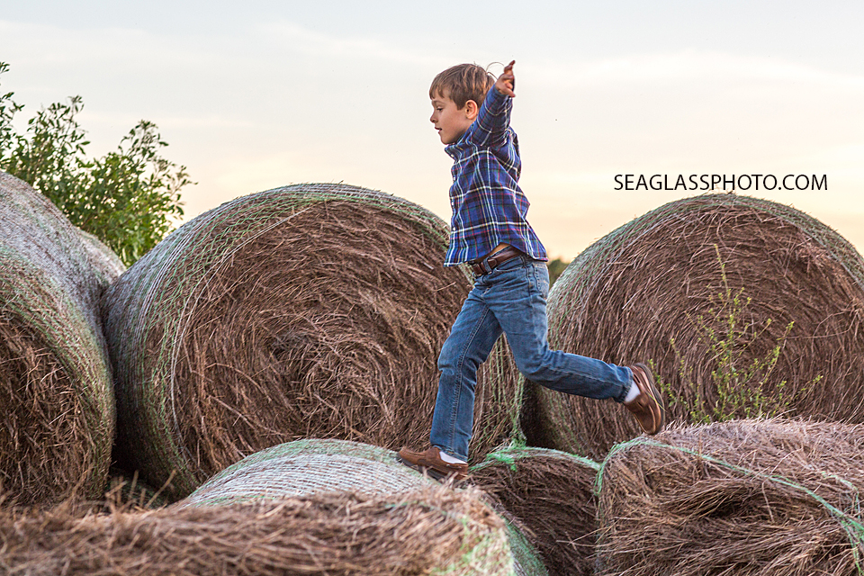 Boy with blue plaid shirt jumping from hay pile to hay pile in Vero Beach Florida