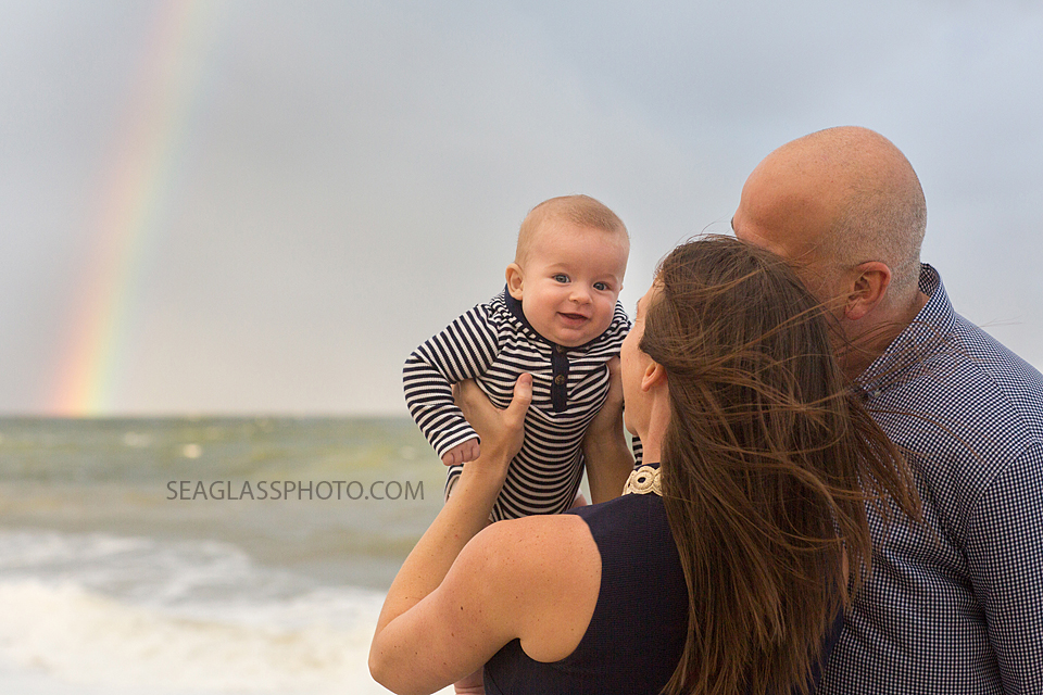 parents holding baby boy at the beach looking at a rainbow in Vero Beach Florida family photography