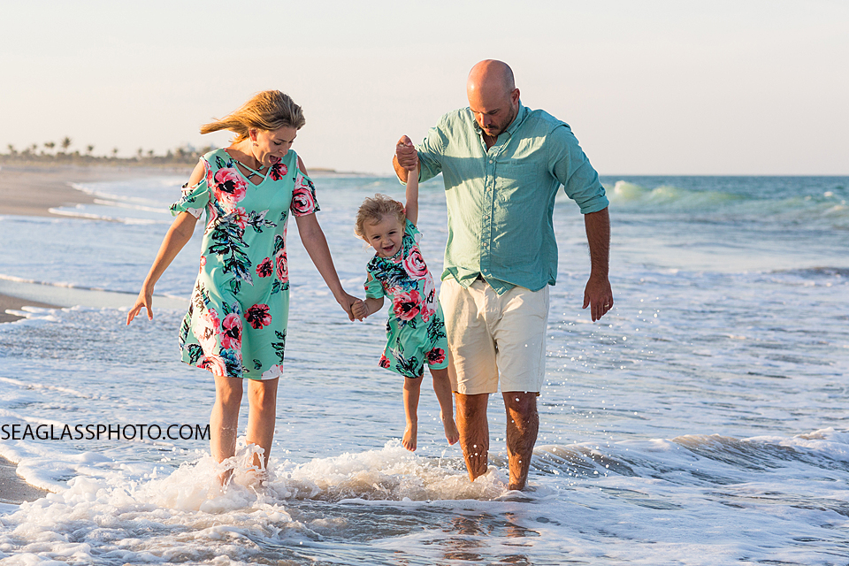 Family wading in the water of the ocean, Parents swinging their young daughter over the water during family photos in Vero Beach Florida