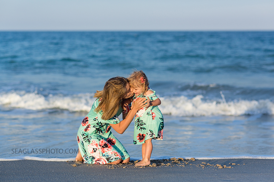 Mother bent down to kiss daughters face on the beach wearing matching outfits during family photos in Vero Beach Florida