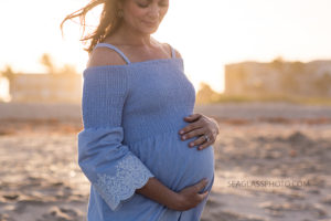 Pregnant mom holding her unborn child wearing blue on the beach during maternity photos in Vero Beach Florida