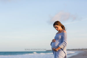 Pregnant mom holding her unborn child on the beach at sunset during maternity photos in Vero Beach Florida
