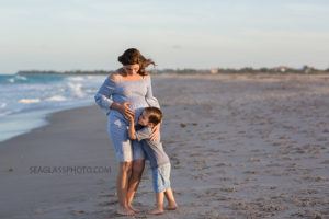 Young boy hugging his mom and unborn sibling during maternity photos on the beach in Vero Beach Florida