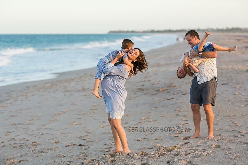 Pregnant mother holding oldest son while father plays with younger son on the beach during maternity photos in Vero Beach Florida