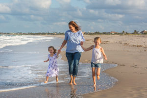 mom walking with her daughter along the waters edge on the beach laughing during family photo shoot in Vero Beach Florida