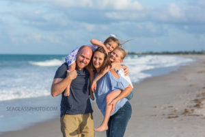 Parents holding their daughters on their backs while the girls hug each other during family photo shoot on the beach in Vero Beach Florida