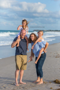 A vertical photo of a family posing for a picture in front of the water on the beach in Vero Beach Florida