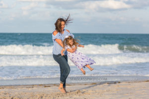 Mom swinging her youngest daughter on the beach during family photo shoot in Vero Beach Florida