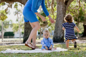 Little boy looking at the camera while big sister runs past and mom tries to catch her during family photos at Riverside park in Vero Beach Florida