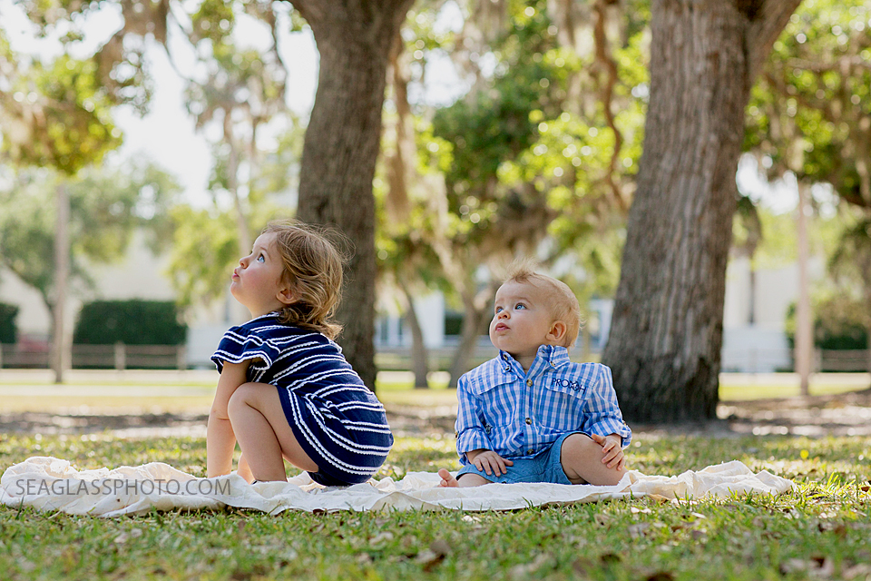 Big sister and little brother focus on something behind scenes during family photo shoot at Riverside park in Vero Beach Florida