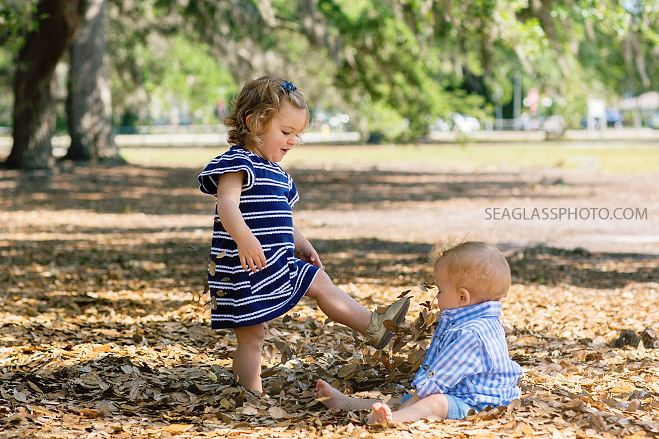 Big sister kicks up leaves next to little brother at Riverside Park in Vero Beach Florida