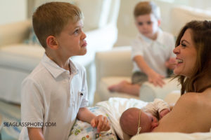 Close up of older brother pouting as his mom nurses his little sister while laughing during newborn shoot in Vero Beach Florida