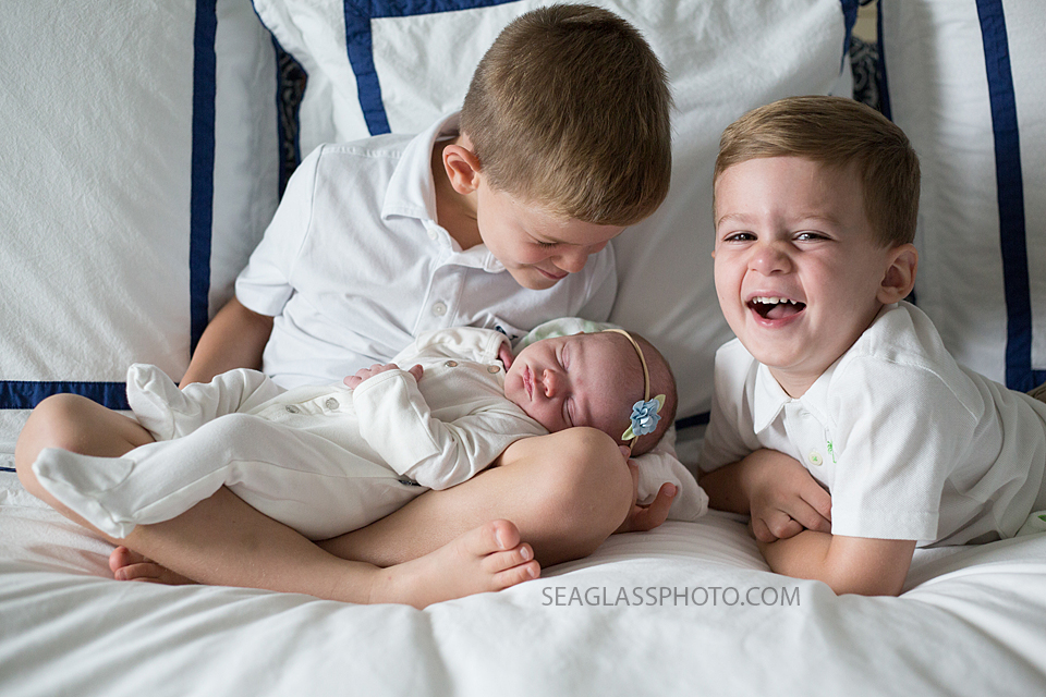 Older brothers laughing as they hold and goof around with their little sister during newborn shoot in Vero beach Florida