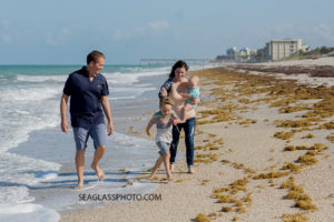 Family walks by the water on the beach while the son tries not to touch the water during family photos in Vero Beach Florida