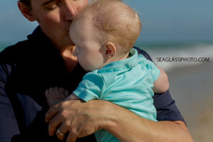 Close up of dad kissing his youngest sons forehead on the beach during family photos in Vero Beach Florida