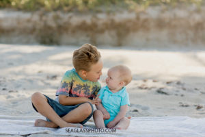 Brothers look at each other while sitting on the beach during family photos in Vero Beach Florida