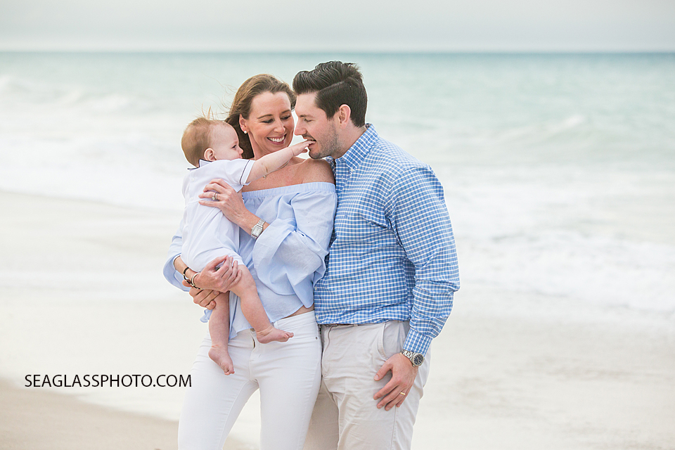 Father play bites sons hand as mom holds him on the beach at Johns island beach club during family photos in Vero Beach Florida