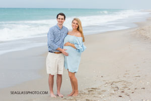 Husband and expecting wife pose on the beach at johns island beach club during family photos in Vero Beach Florida