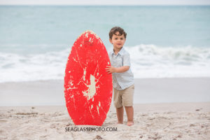Little boy poses with a skim board on the beach at johns island beach club during family photos in Vero Beach Florida