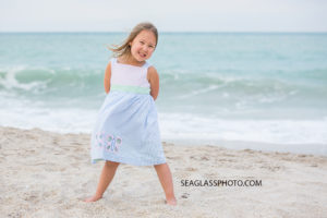 Little girl poses on the beach in front of the waves at johns island beach club during family photos in Vero Beach Florida