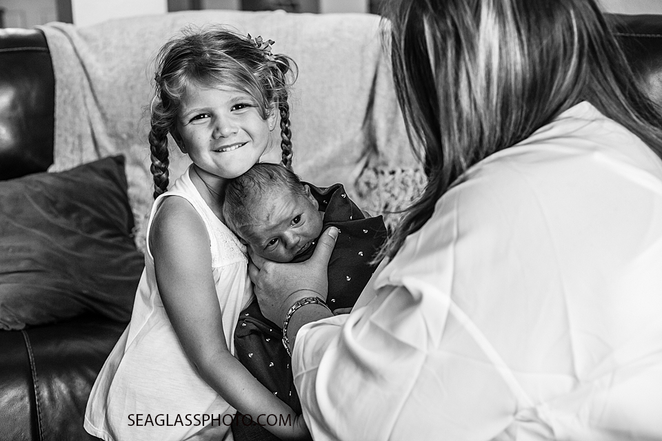 Older sister hugs her newborn baby brother as mom holds him during newborn shoot in Vero Beach Florida