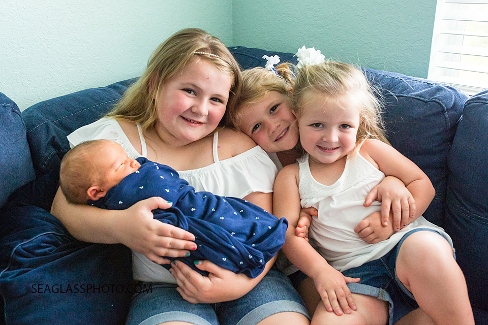 Three older sisters hold their newborn baby brother during newborn shoot in Vero Beach Florda