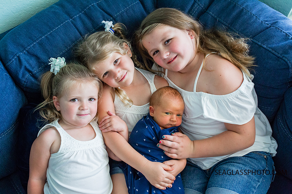 Three older sister look up as they pose with their little brother during newborn shoot in Vero Beach Florida