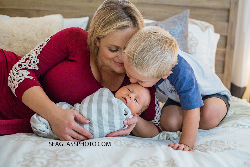 Big brother kisses new little brothers fore head while mommy holds him during newborn session in Vero Beach Florida