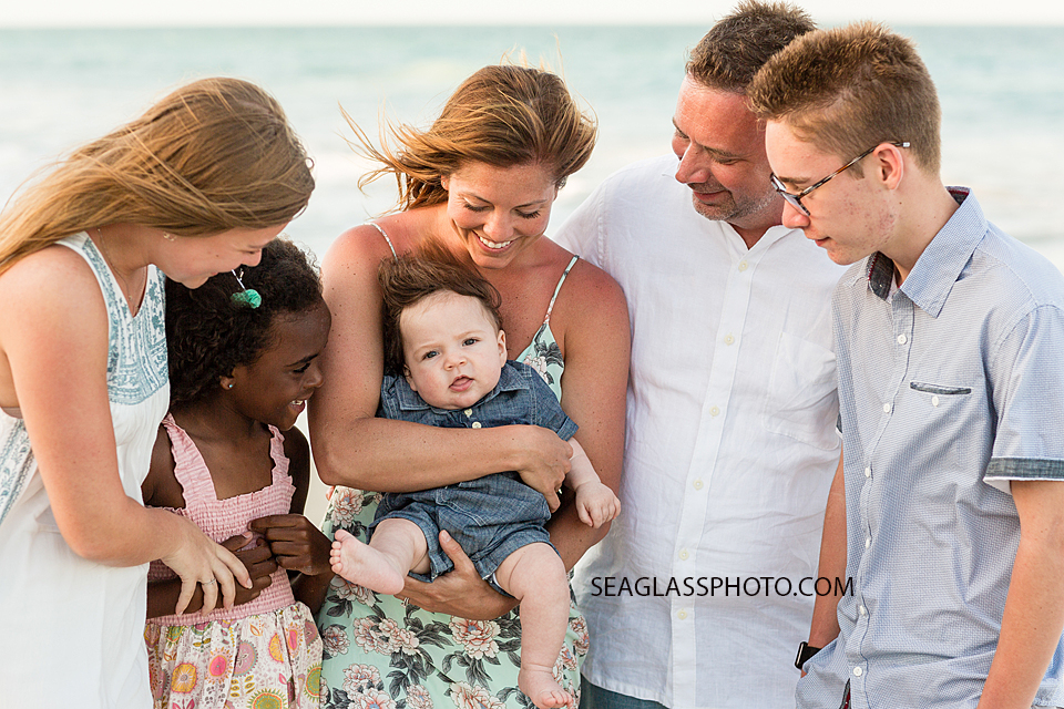 Family smile at the newest addition to the family on the beach during gamily photo shoot in Vero Beach Florida
