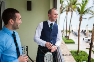 Soon to be husband wearing navy and a kilt talks to one of his groomsmen and has a drink before the wedding at the Kimpton Vero Beach Hotel and Spa in Vero beach florida