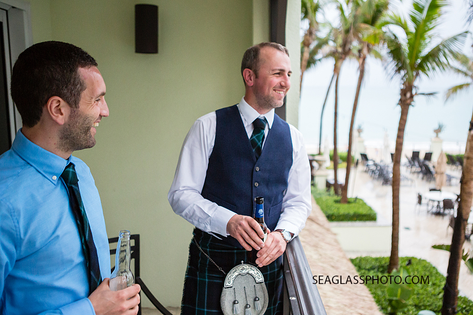 Soon to be husband wearing navy and a kilt talks to one of his groomsmen and has a drink before the wedding at the Kimpton Vero Beach Hotel and Spa in Vero beach florida