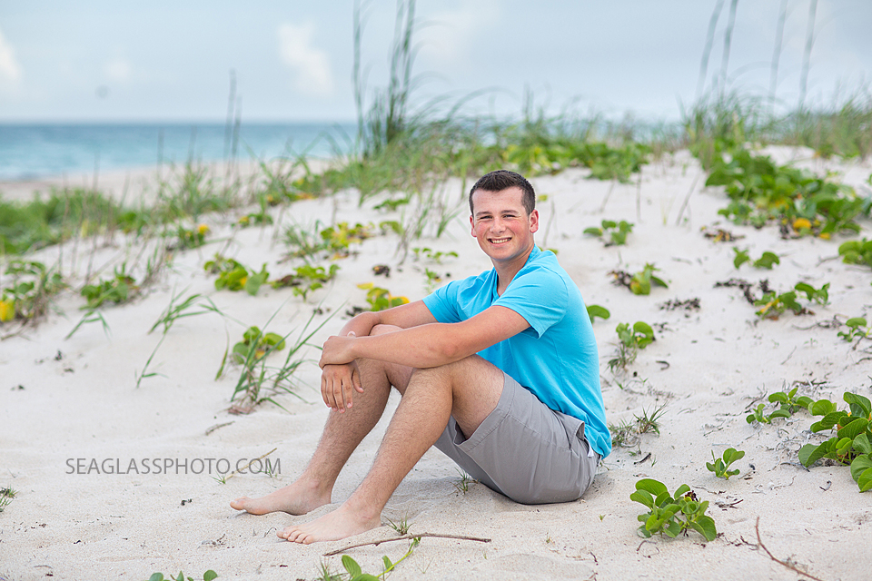 Soon to be senior sits near the dunes on the beach for his senior pictures in Vero Beach Florida
