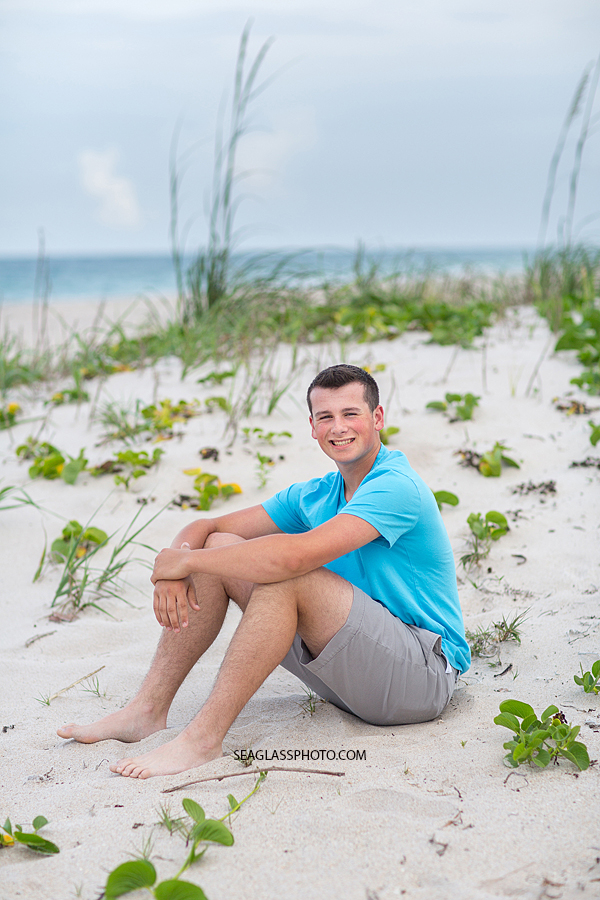 young man sits in the dunes for his senior pictures in Vero Beach Florida