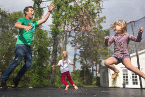 Dad jumps on the trampoline with his two daughters during a home photo shoot in Vero Beach Florida