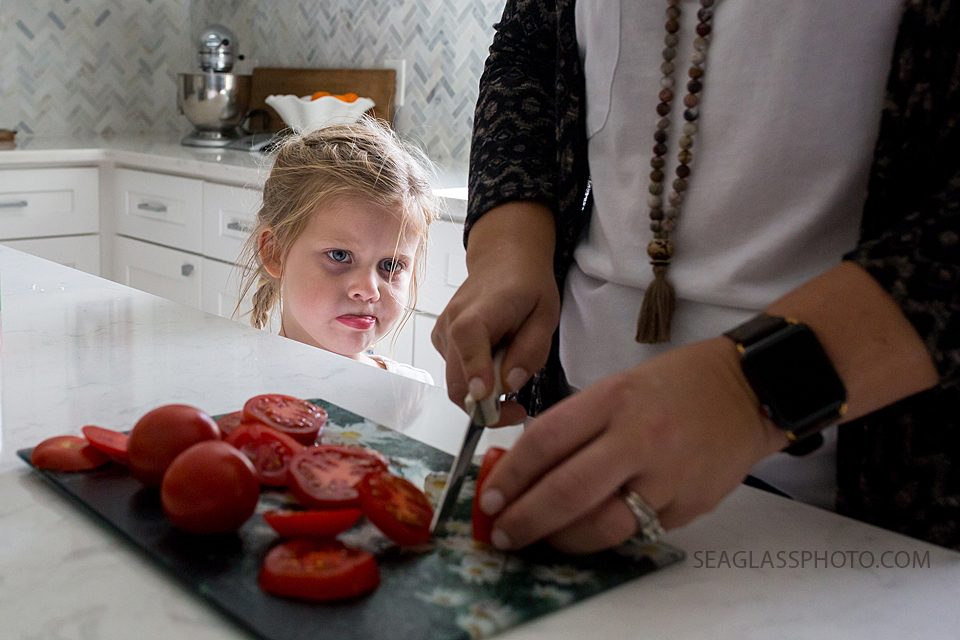 Close up of mom cutting tomatoes and youngest daughter watching during a home photo shoot in Vero Beach Florida