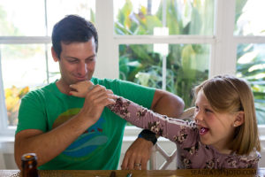 Oldest daughter messes around with her dad at the dinner table during a home photo shoot in Vero Beach Florida