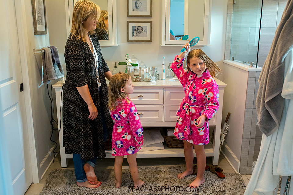 Oldest sister combs her hair after bath time while wearing matching robes with her sister during a home photo shoot in Vero Beach Florida