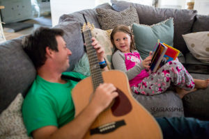 Daughter reads her father a story while he plays the guitar during a home photo shoot in Vero Beach Florida
